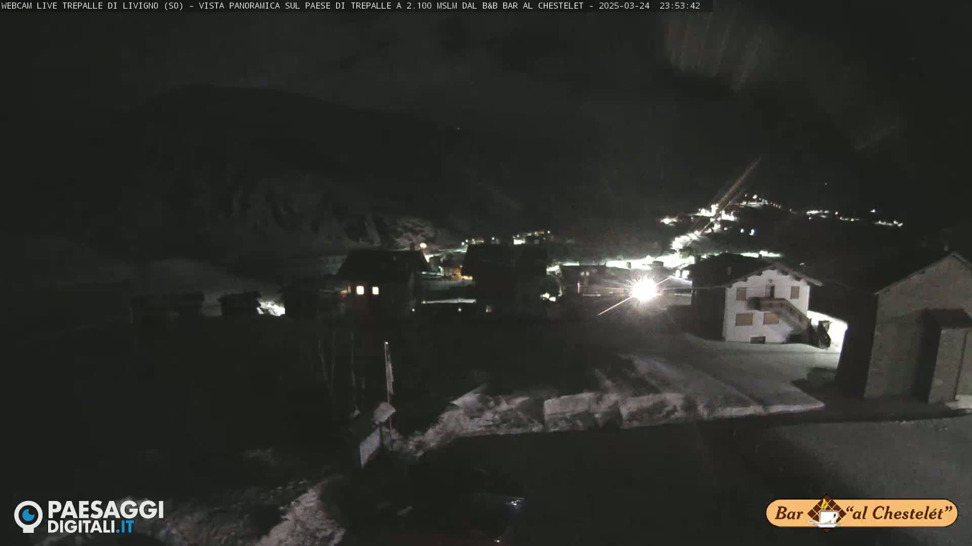 A nighttime view of a snow-covered village nestled in a dark, mountainous area.