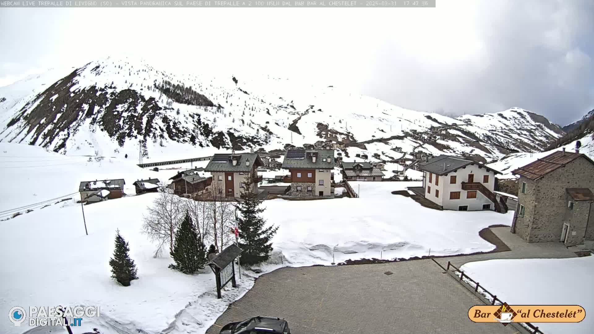 A snow-covered village nestled in a valley surrounded by snow-capped mountains under an overcast sky.