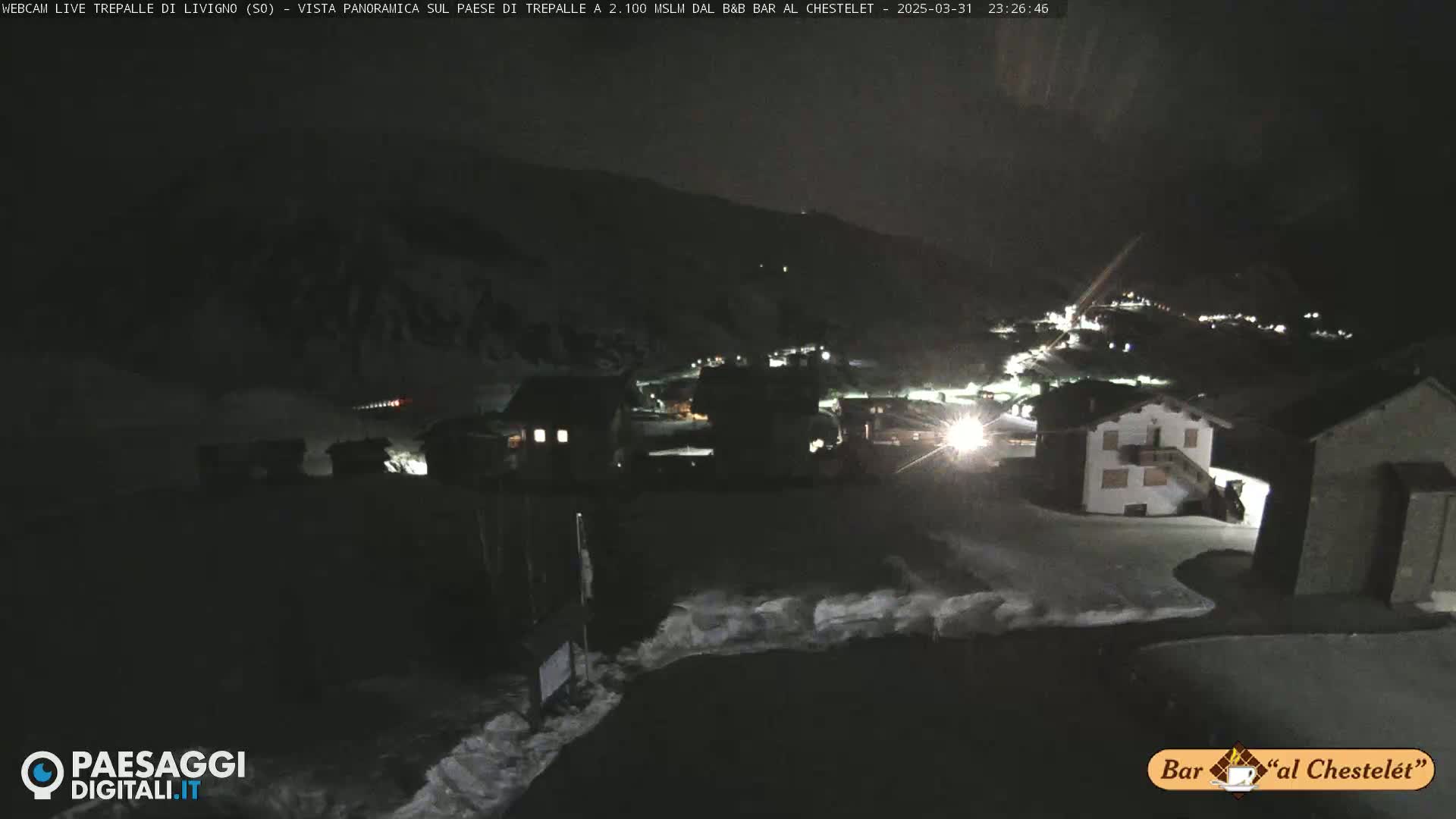 A nighttime, snow-covered village nestled in a mountain valley under a dark sky.