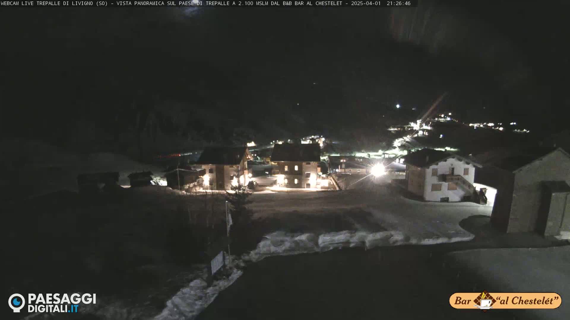 A nighttime view of a snow-covered village with several illuminated buildings under a dark sky.