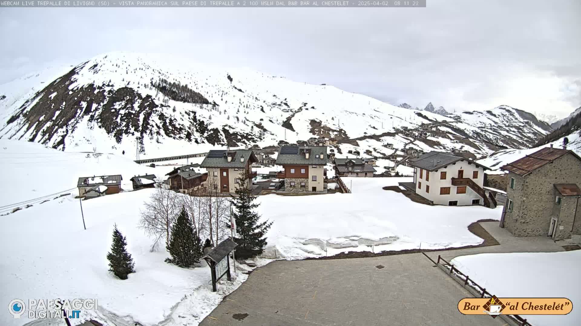 A snow-covered village nestled in a valley between snow-capped mountains under an overcast sky.