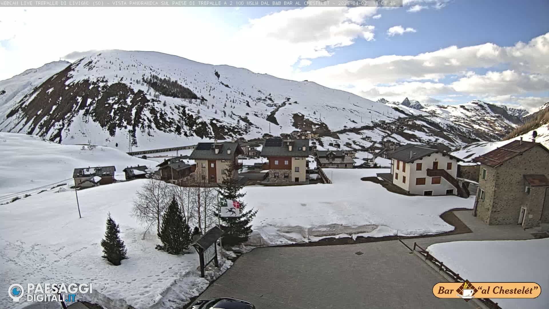 A snow-covered village nestled in a valley between snow-dusted mountains under a partly cloudy sky.