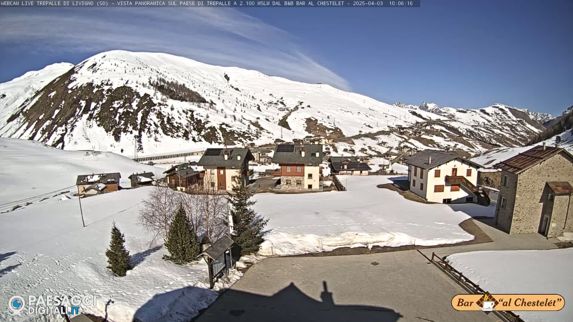 A snow-covered village nestled in a valley surrounded by snow-capped mountains under a clear blue sky.
