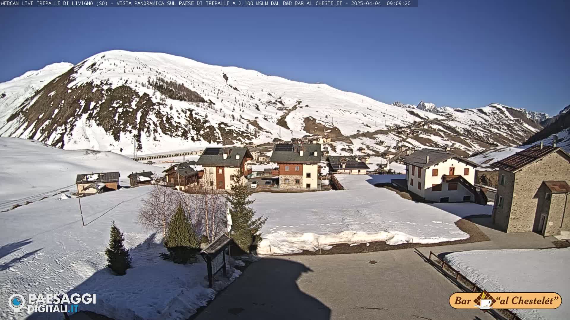 A snow-covered village nestled in a valley between snow-capped mountains on a sunny day.