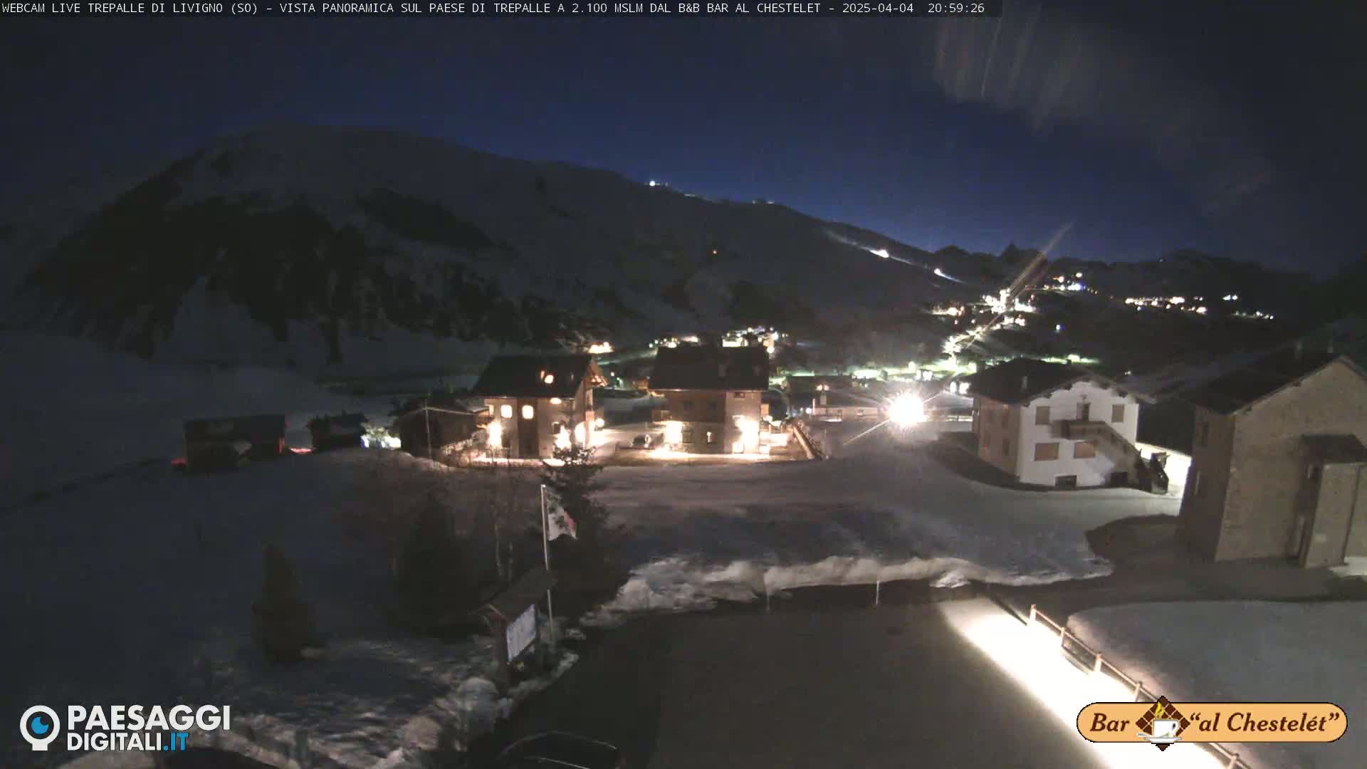 A snow-covered village is illuminated at night under a dark sky.