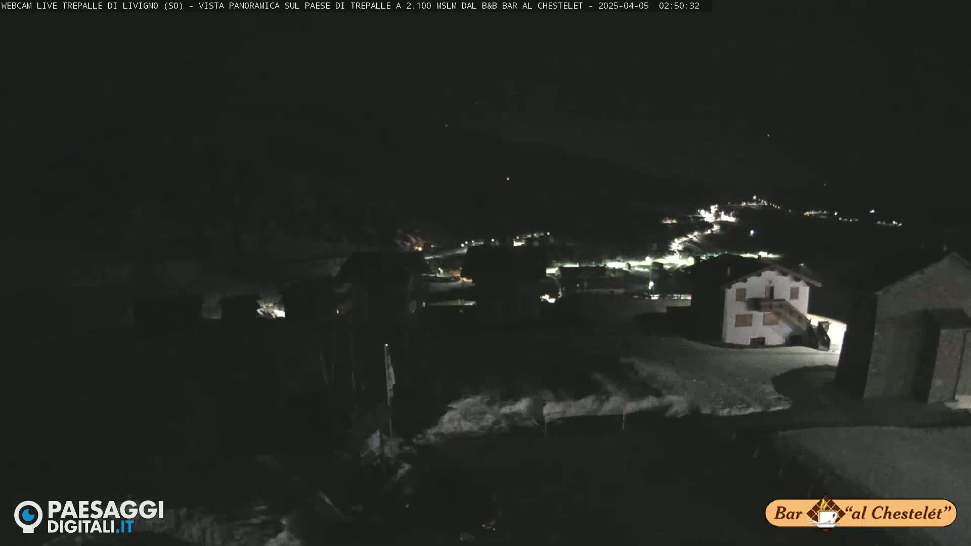 A nighttime, snowy landscape showing a village with scattered lights under a dark sky.