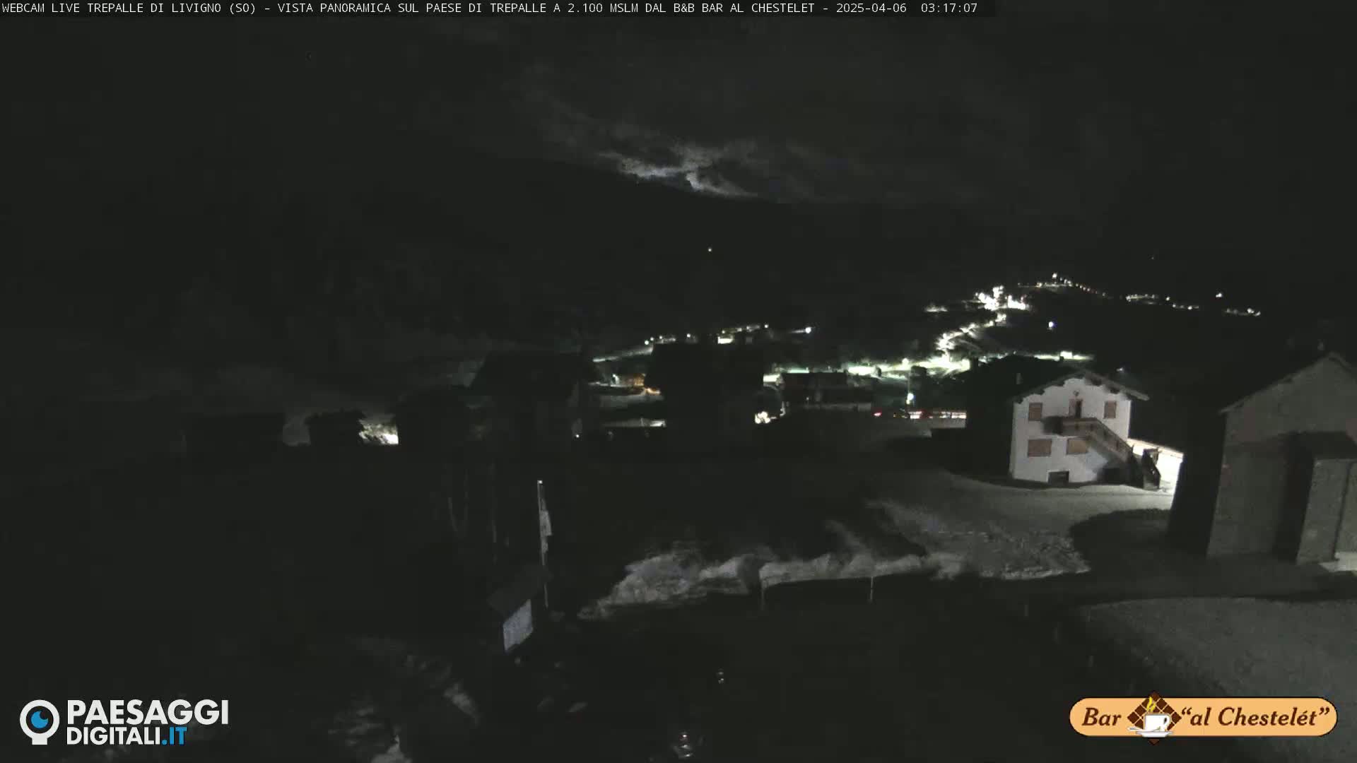 A nighttime, snow-covered village is seen under a cloudy sky.