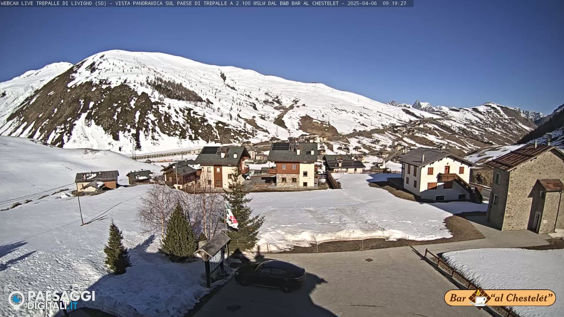 A snow-covered village nestled in a valley surrounded by snow-capped mountains under a clear blue sky.