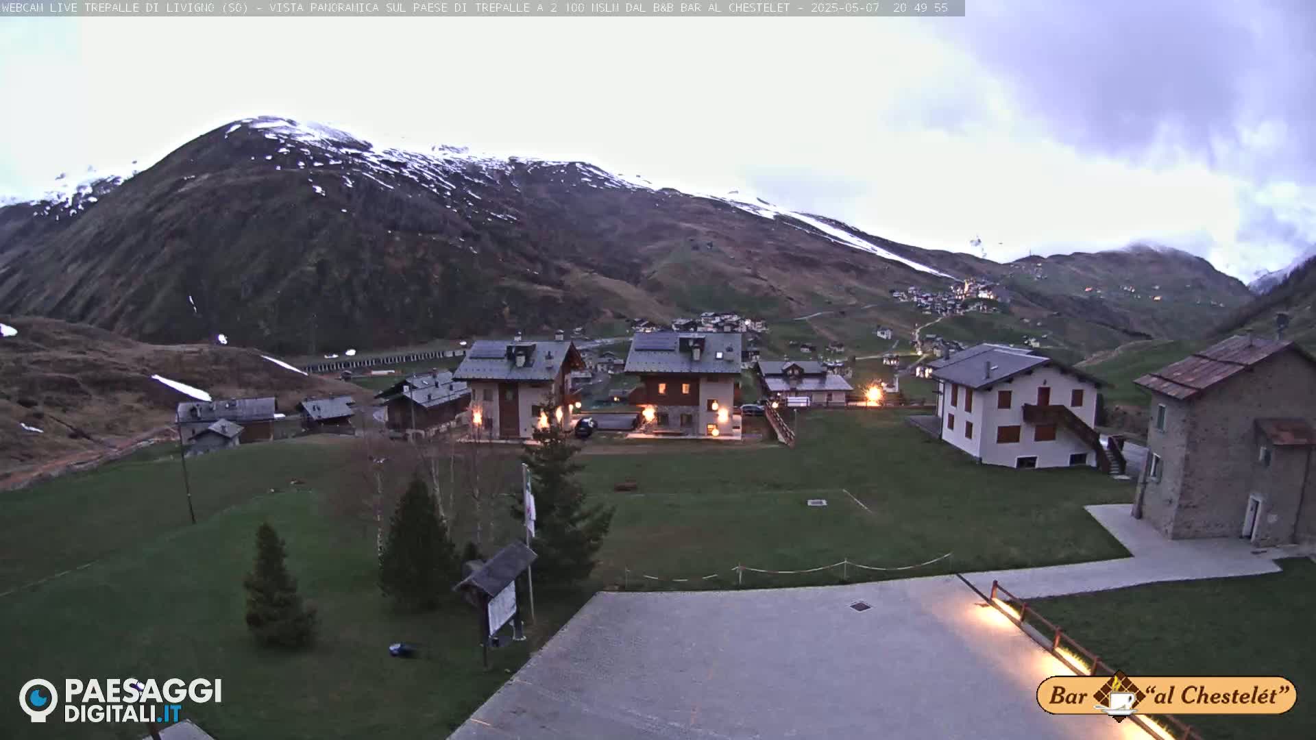 A small village nestled in a valley between snow-capped mountains under a twilight sky.