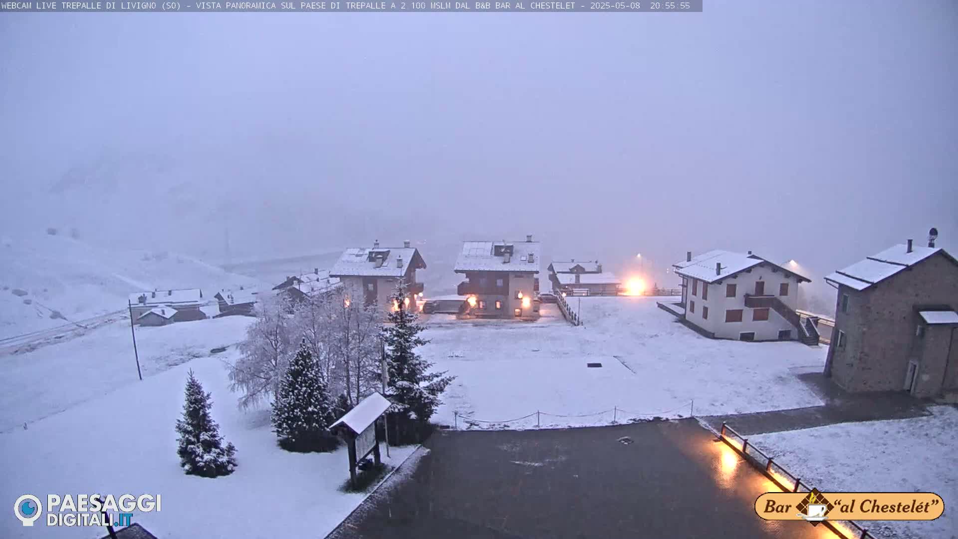 A snow-covered village with several buildings is visible under a hazy, overcast sky.