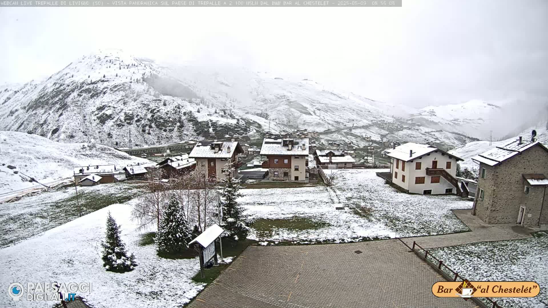A snow-covered village nestled in a mountainous region, with light snowfall.