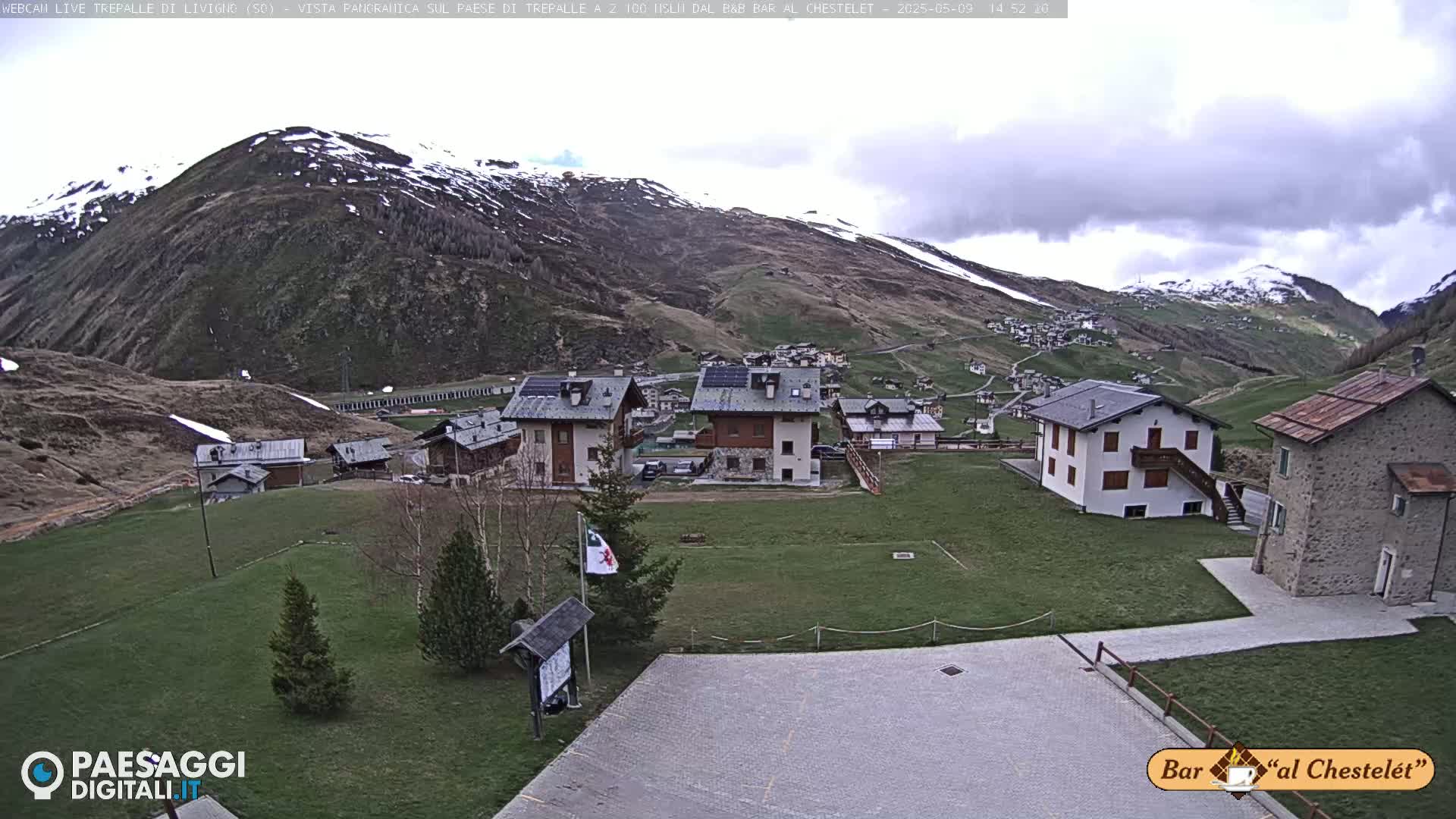 A small village nestled in a valley surrounded by snow-capped mountains under an overcast sky.