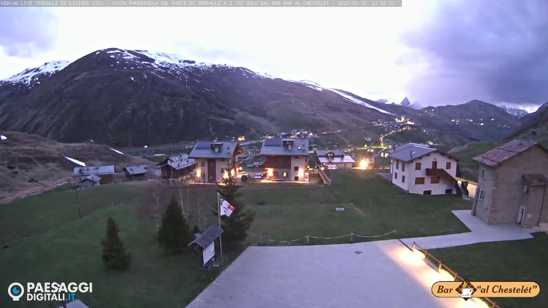 A small village nestled in a valley between snow-capped mountains under a twilight sky.