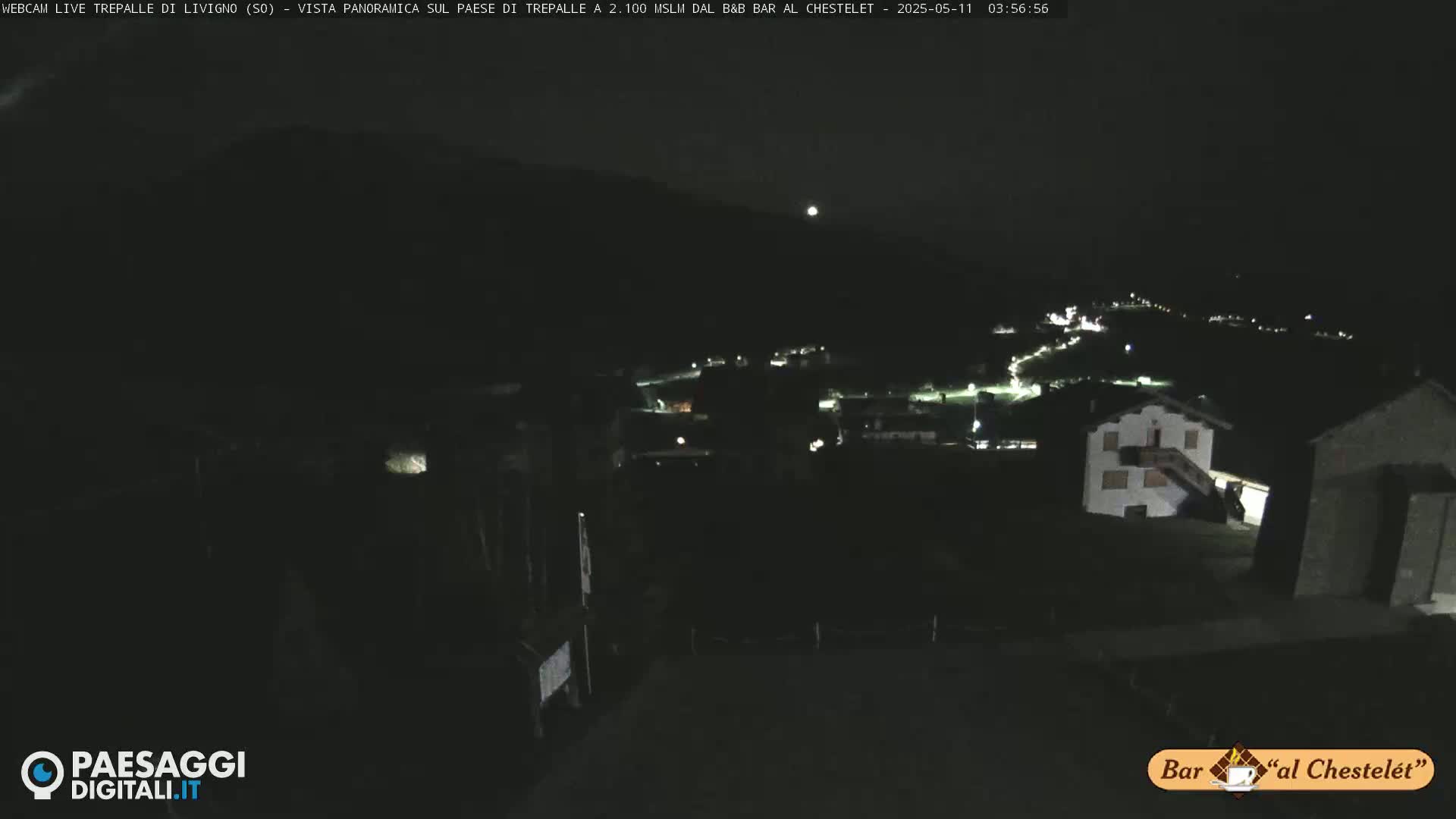 A nighttime, panoramic view of a village nestled in a dark mountain valley under a clear sky.