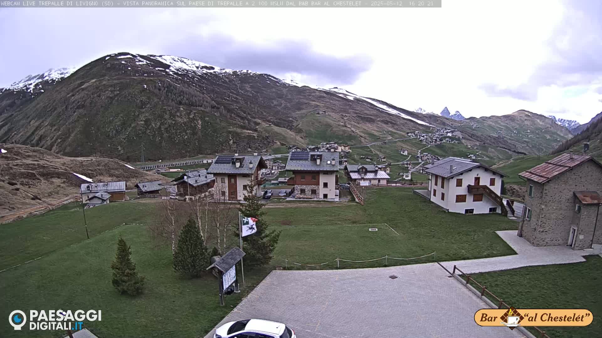 A village nestled in a valley surrounded by snow-capped mountains under an overcast sky.