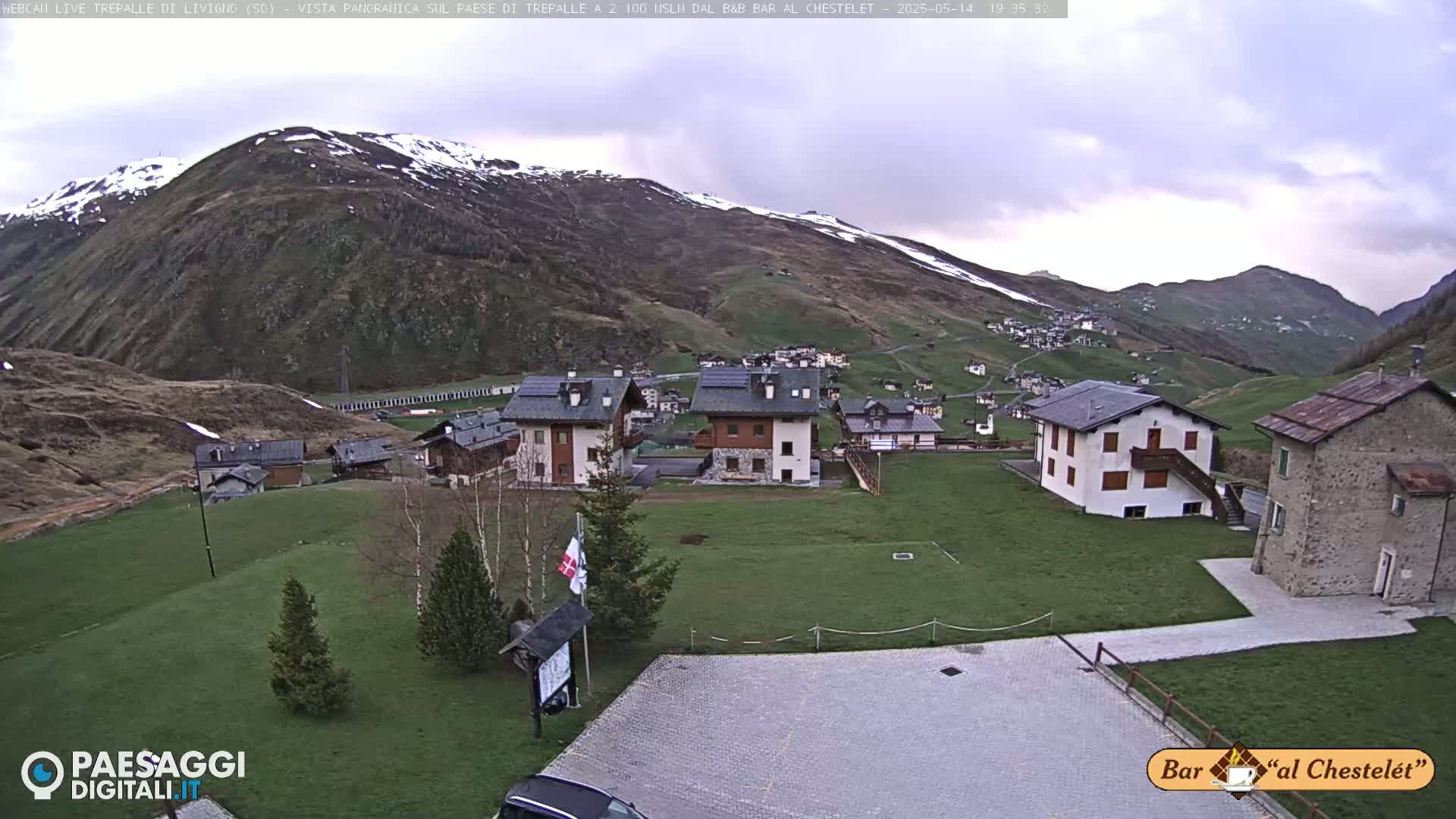 A small village nestled in a valley between snow-dusted mountains under an overcast sky.