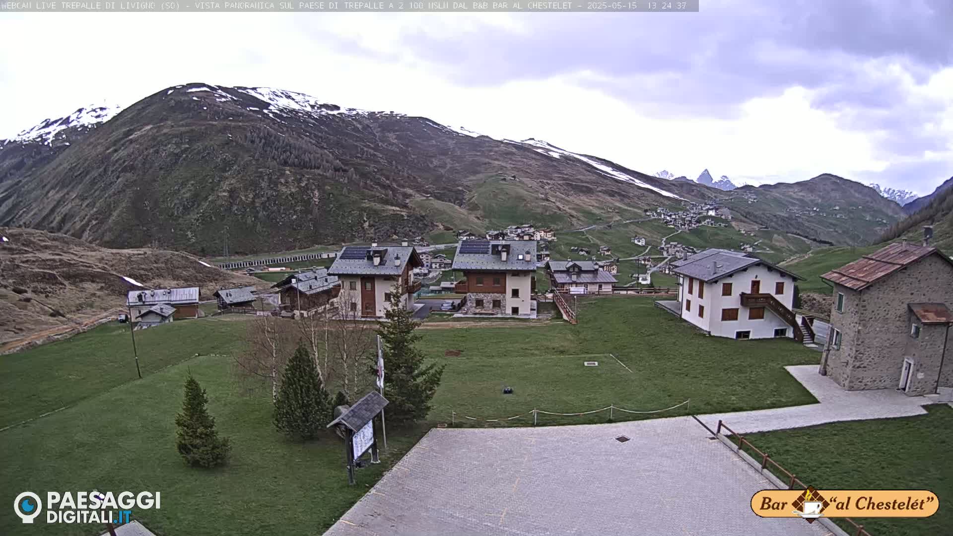 A small village nestled in a valley surrounded by snow-capped mountains under an overcast sky.
