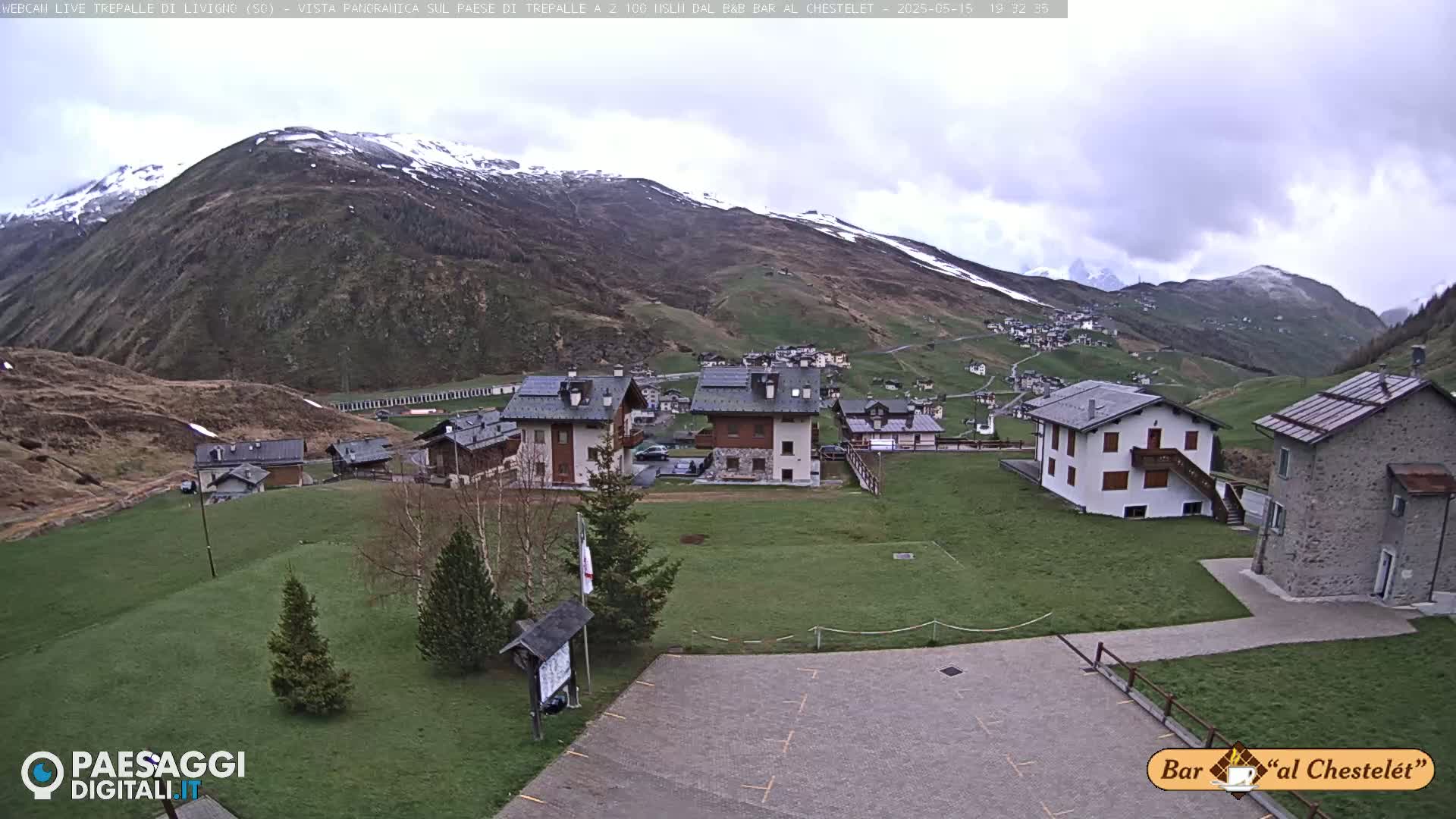 A small village nestled in a valley surrounded by snow-capped mountains under a cloudy sky.