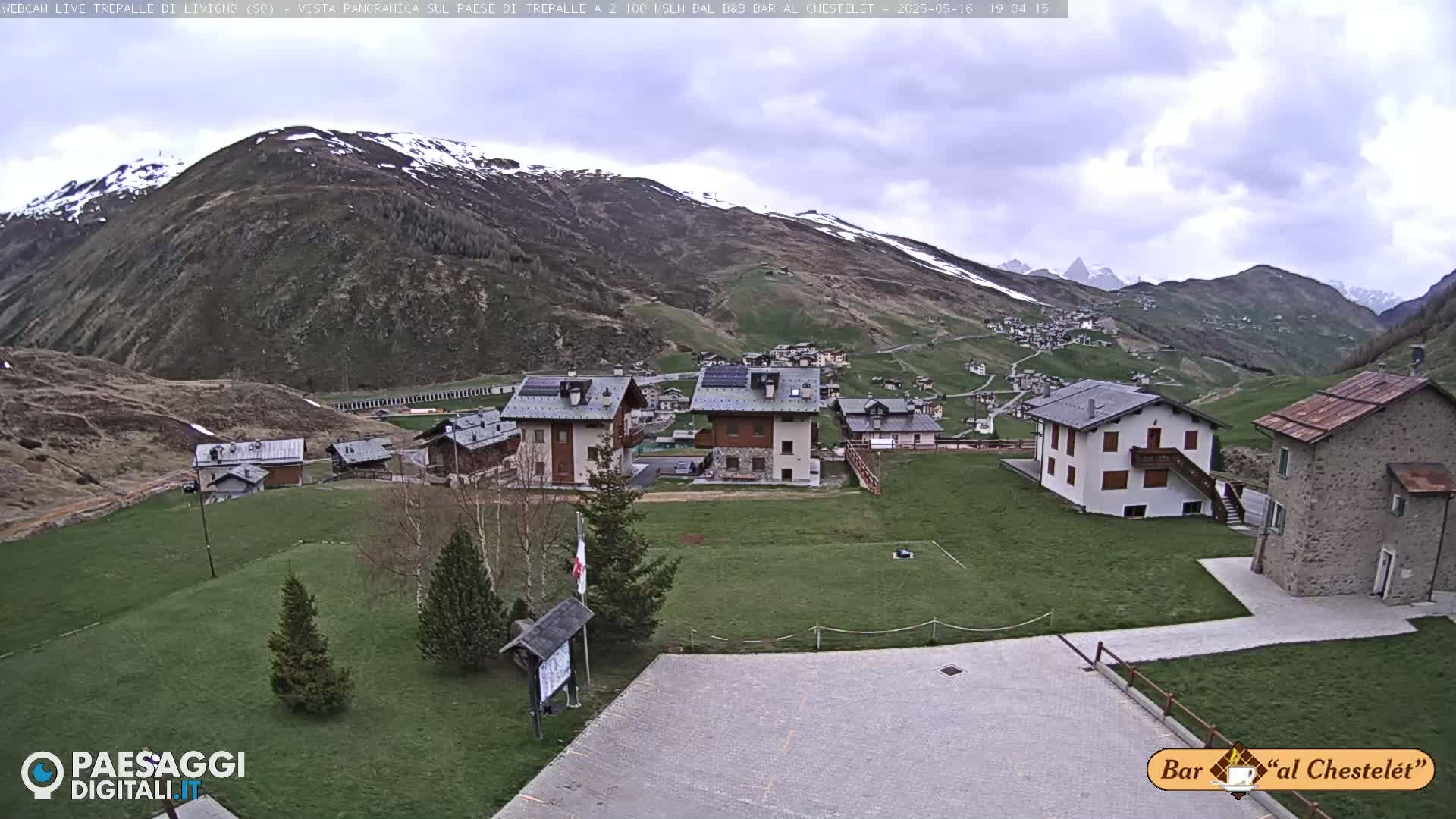 A small village nestled in a valley between snow-capped mountains under a partly cloudy sky.
