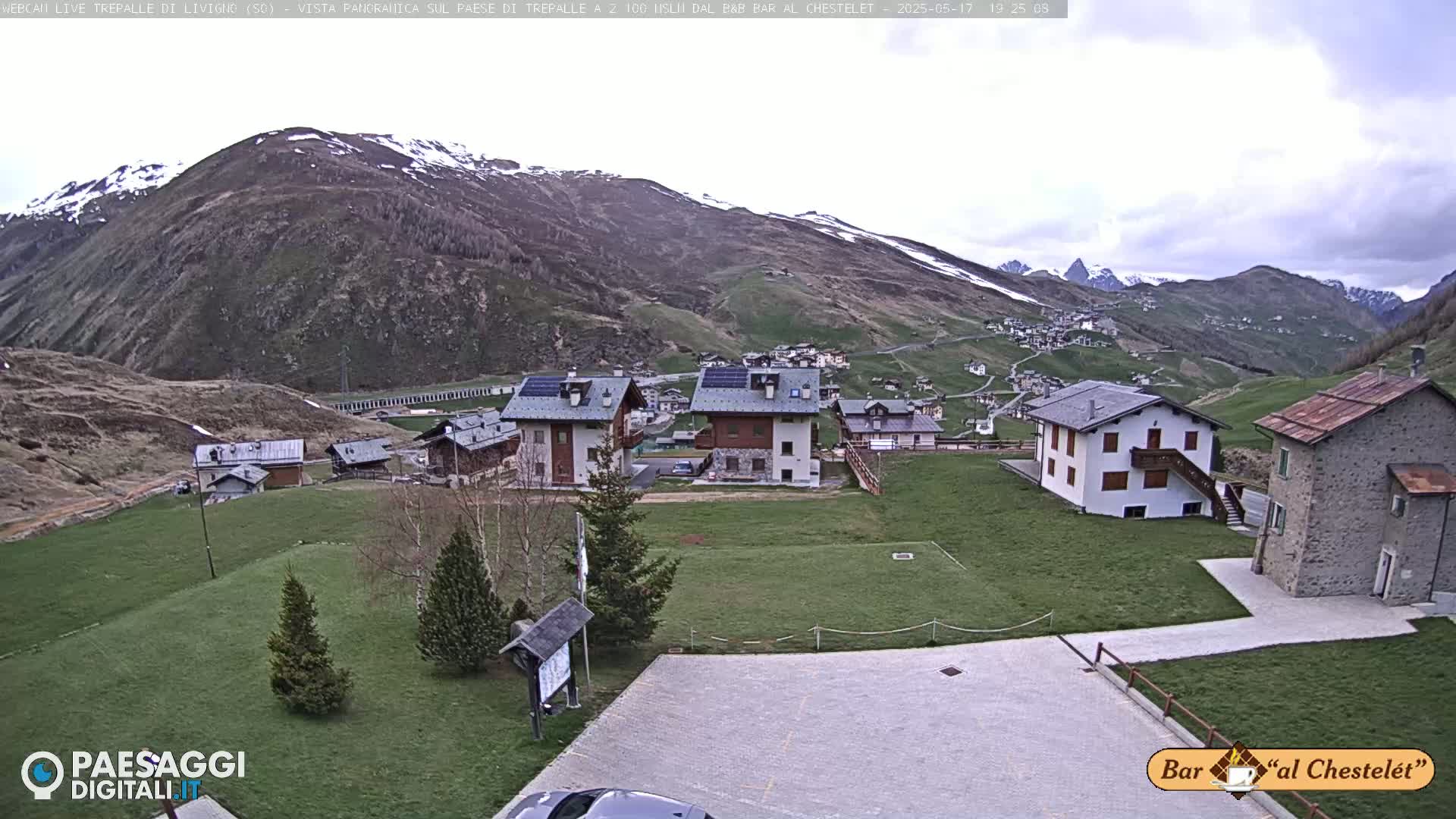 A village nestled in a valley surrounded by snow-capped mountains under an overcast sky.