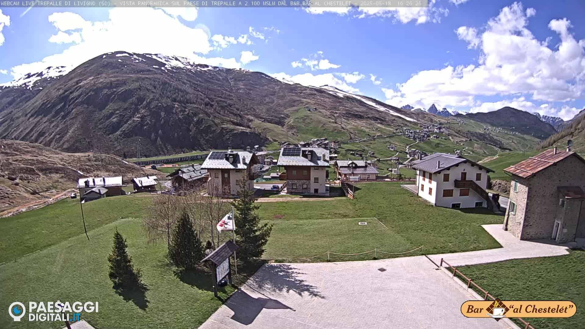 A sunny day reveals a village nestled in a valley surrounded by snow-capped mountains.
