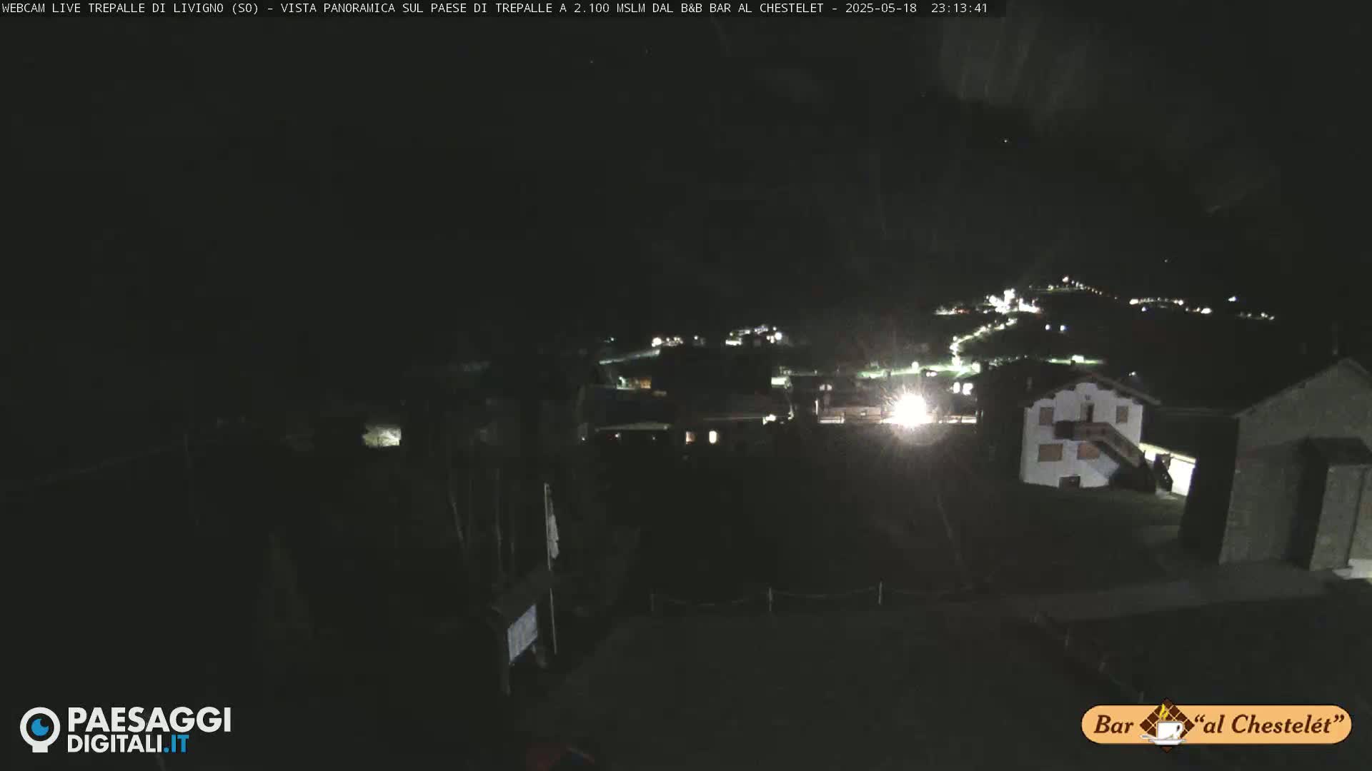 A nighttime, panoramic view of a small village with dimly lit buildings under a dark sky.