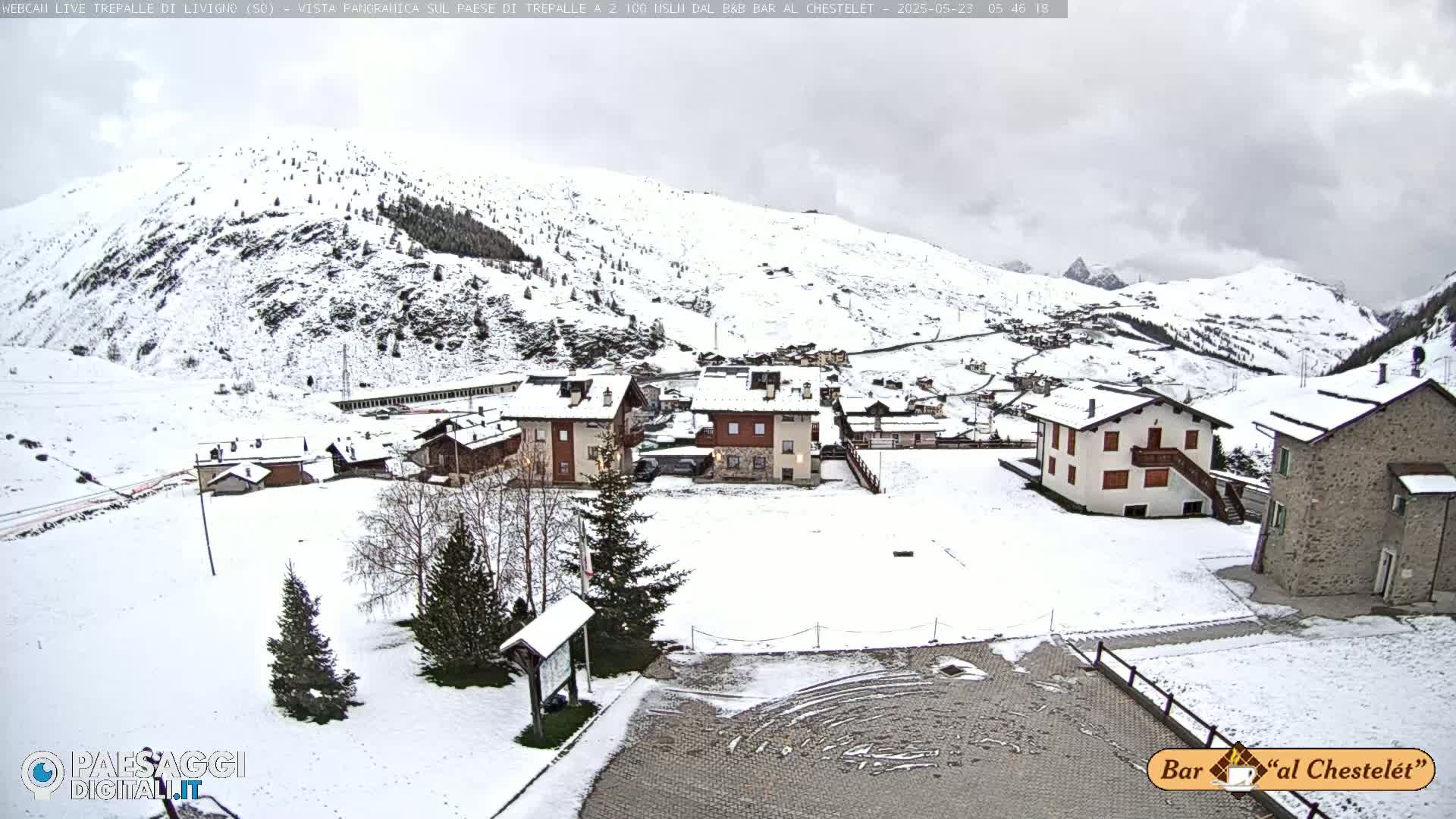 A snow-covered village nestled in a valley surrounded by snow-capped mountains under an overcast sky.