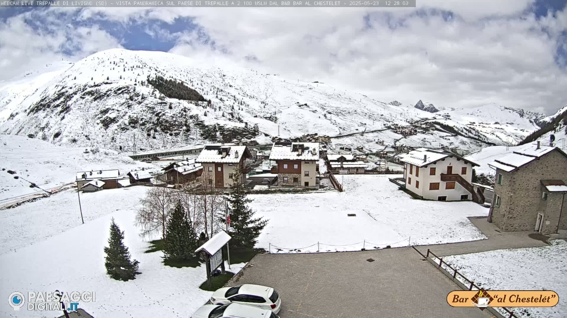 A snow-covered village nestled in a valley, with snow-dusted mountains in the background under a cloudy sky.