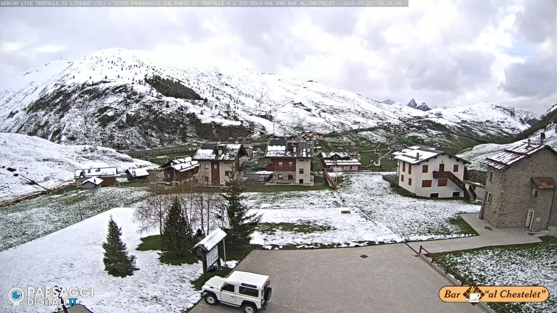 A snow-dusted village nestled in a valley surrounded by snow-covered mountains under a cloudy sky.