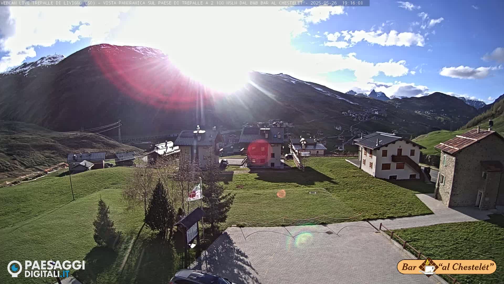 A sunny day with partly cloudy skies reveals a mountain village nestled at the foot of a snow-capped mountain.