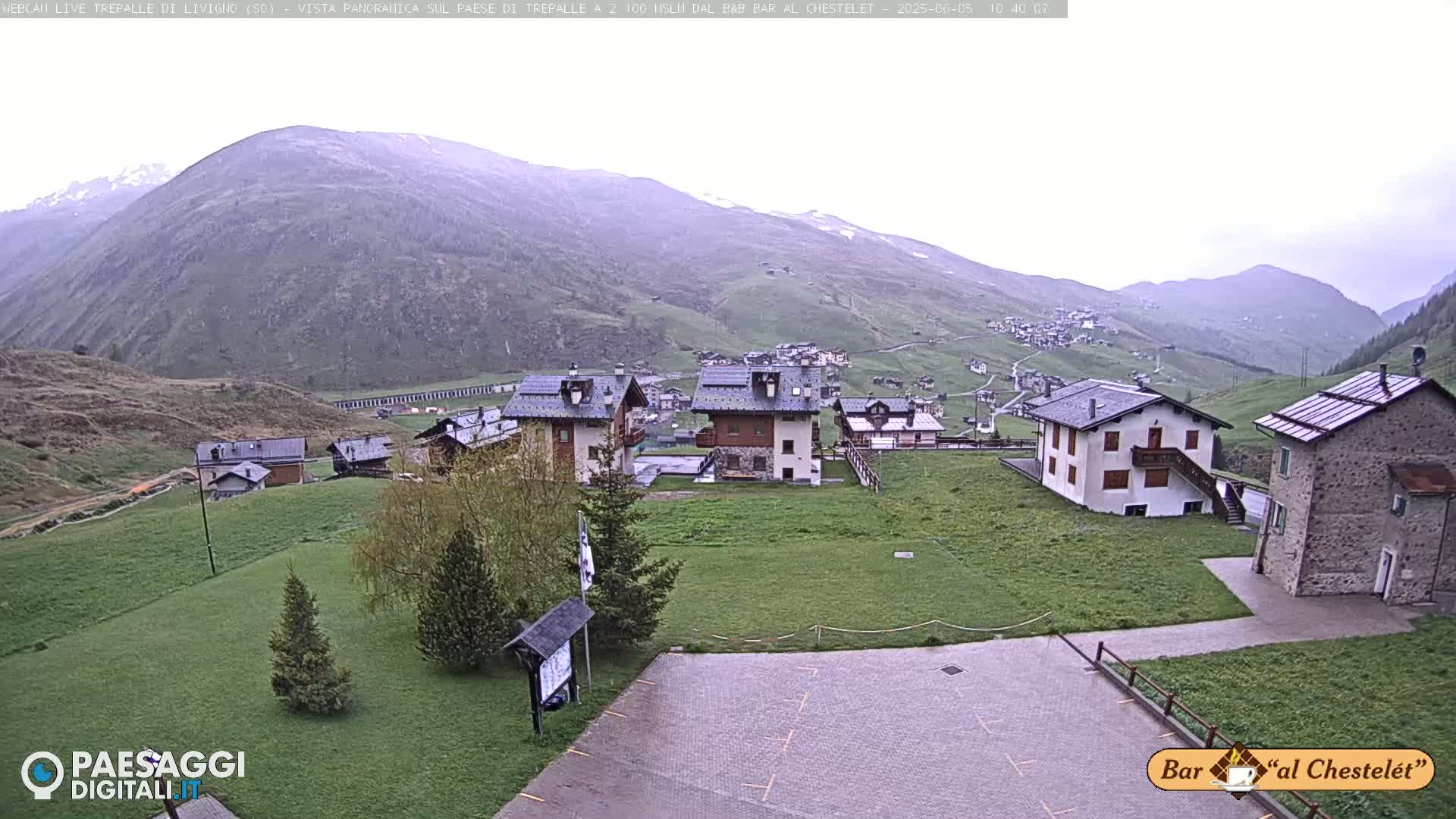 A mountain village with several buildings is visible, nestled in a valley under an overcast sky.