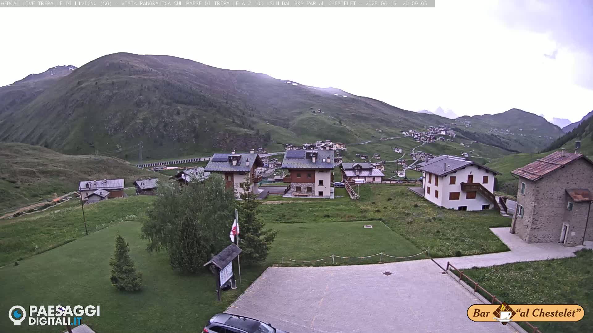 A mountain village with several buildings is nestled in a valley on a partly cloudy day.