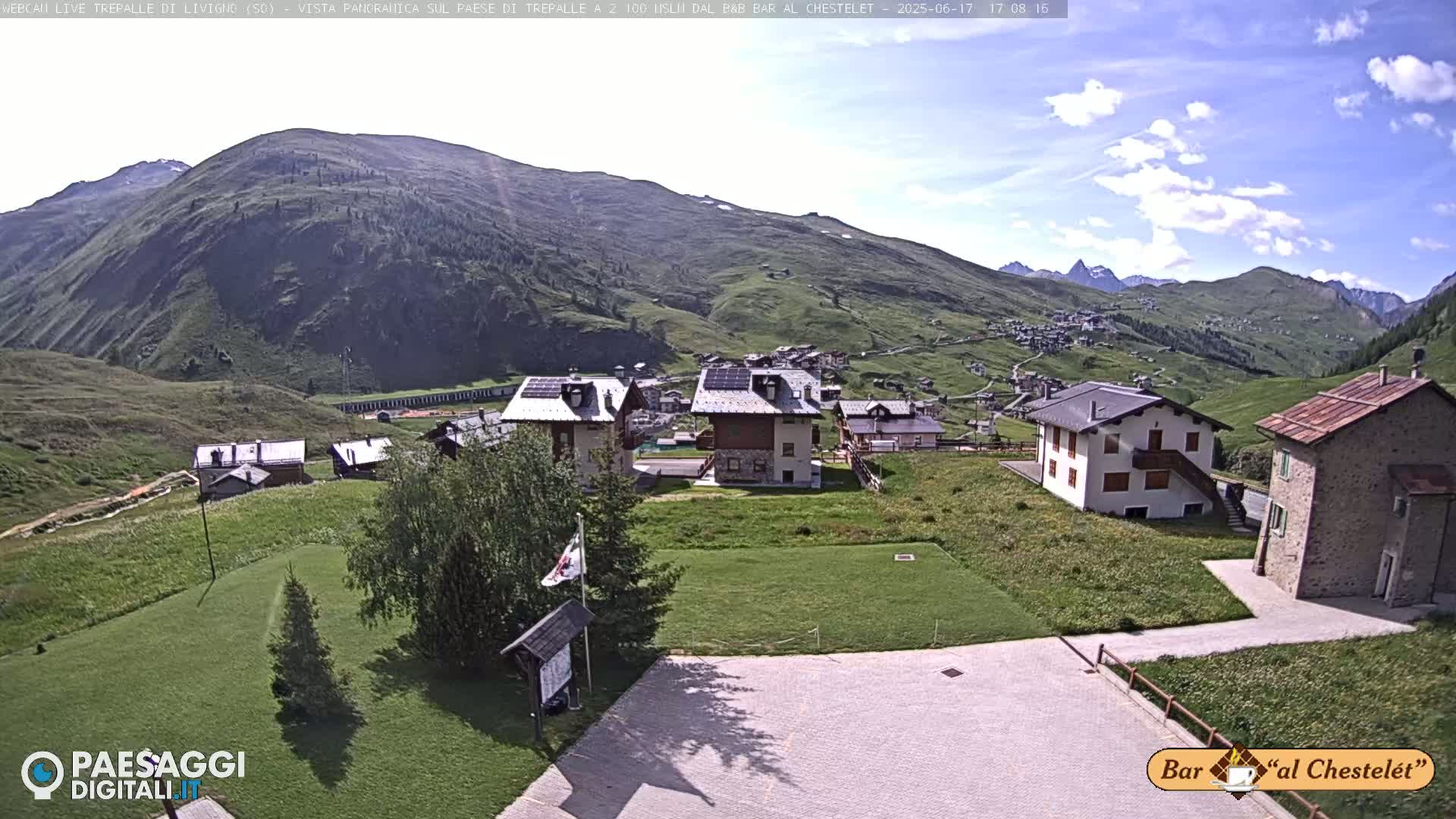 A mountain village nestled in a valley on a sunny day with few clouds.