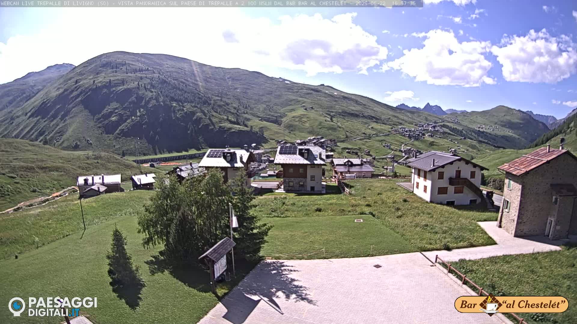 A sunny day reveals a mountain village nestled in a valley, with several buildings and green fields visible.