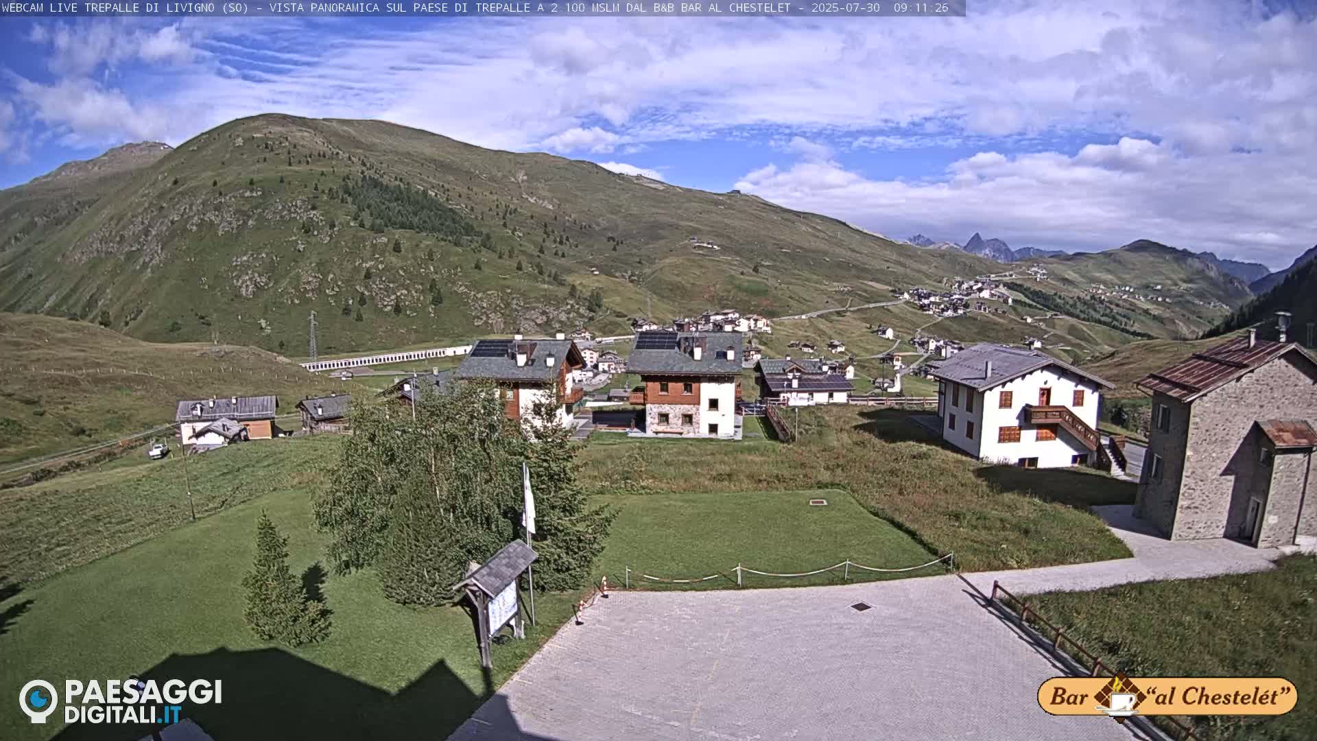 A mountain village nestled in a valley on a partly sunny day, with a few clouds in the sky.