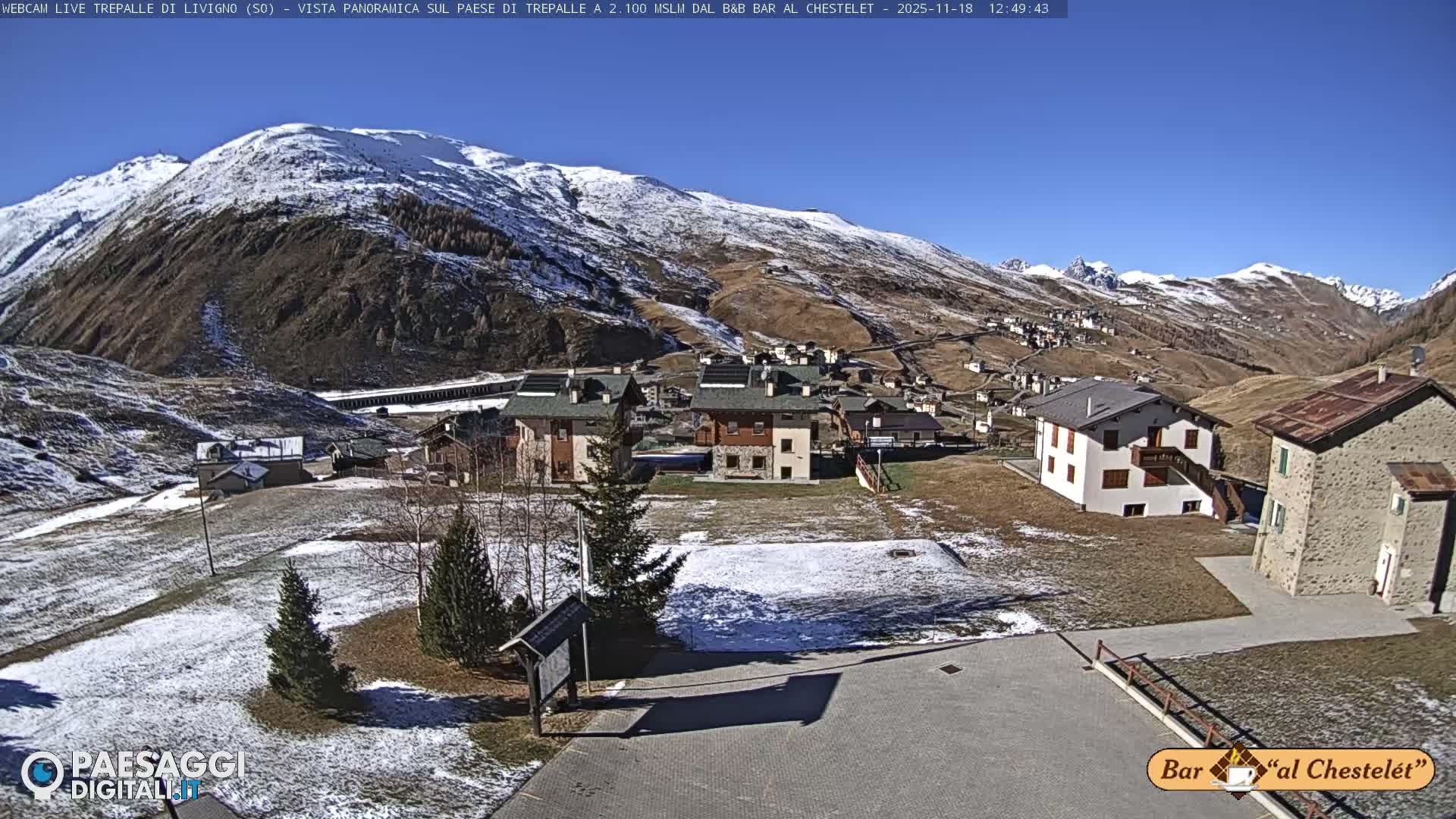 A nighttime view of a snow-dusted mountain village under a clear sky, with scattered lights illuminating buildings and roads across the hilly terrain.