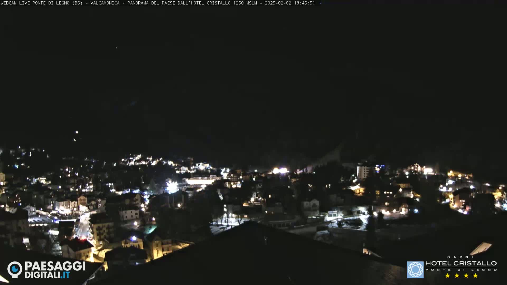 A nighttime, high-angle view of a snow-covered town illuminated by many lights.