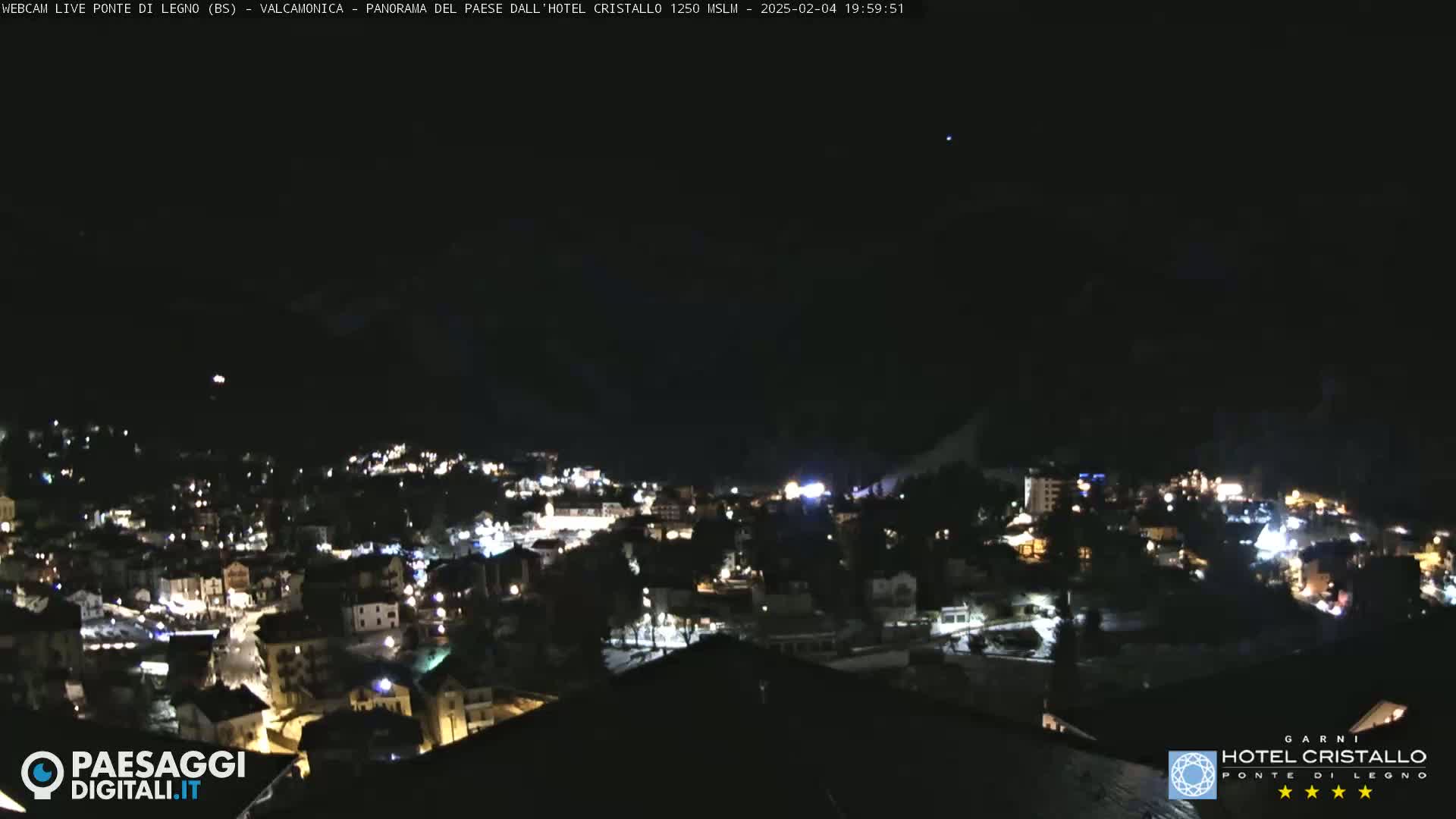 A nighttime view of a town nestled in a valley, illuminated by streetlights under a clear, dark sky.