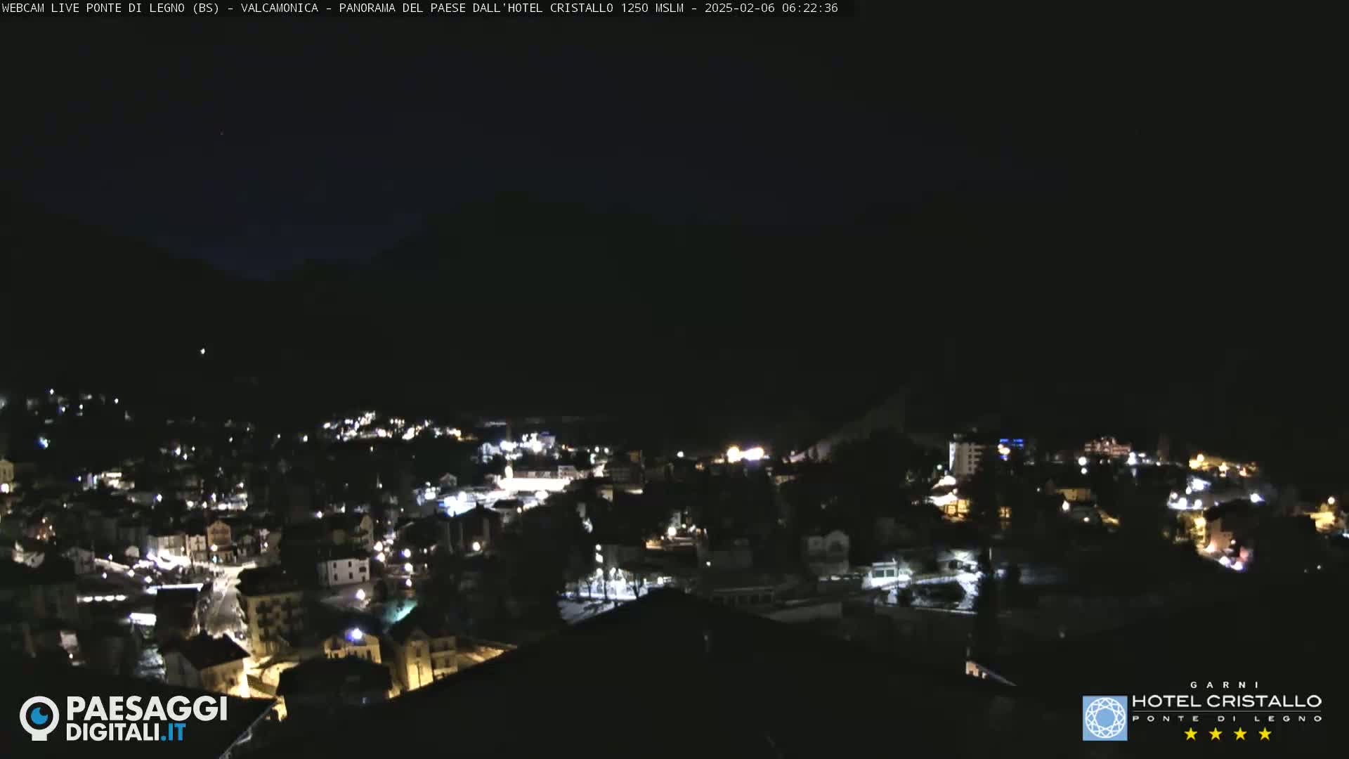 A nighttime view of a town nestled in a valley, illuminated by scattered lights against a dark sky.