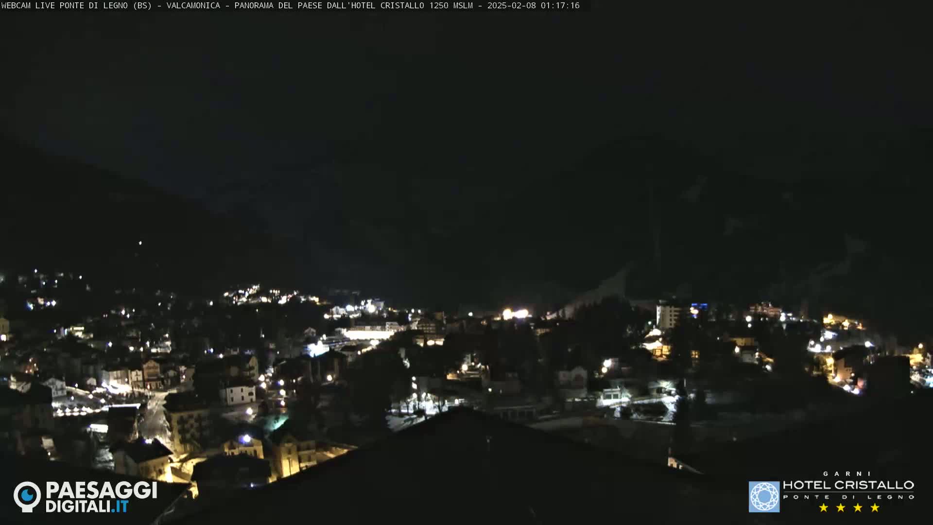 A nighttime, aerial view of a small town nestled in a valley, with mountains in the background under a clear, dark sky.