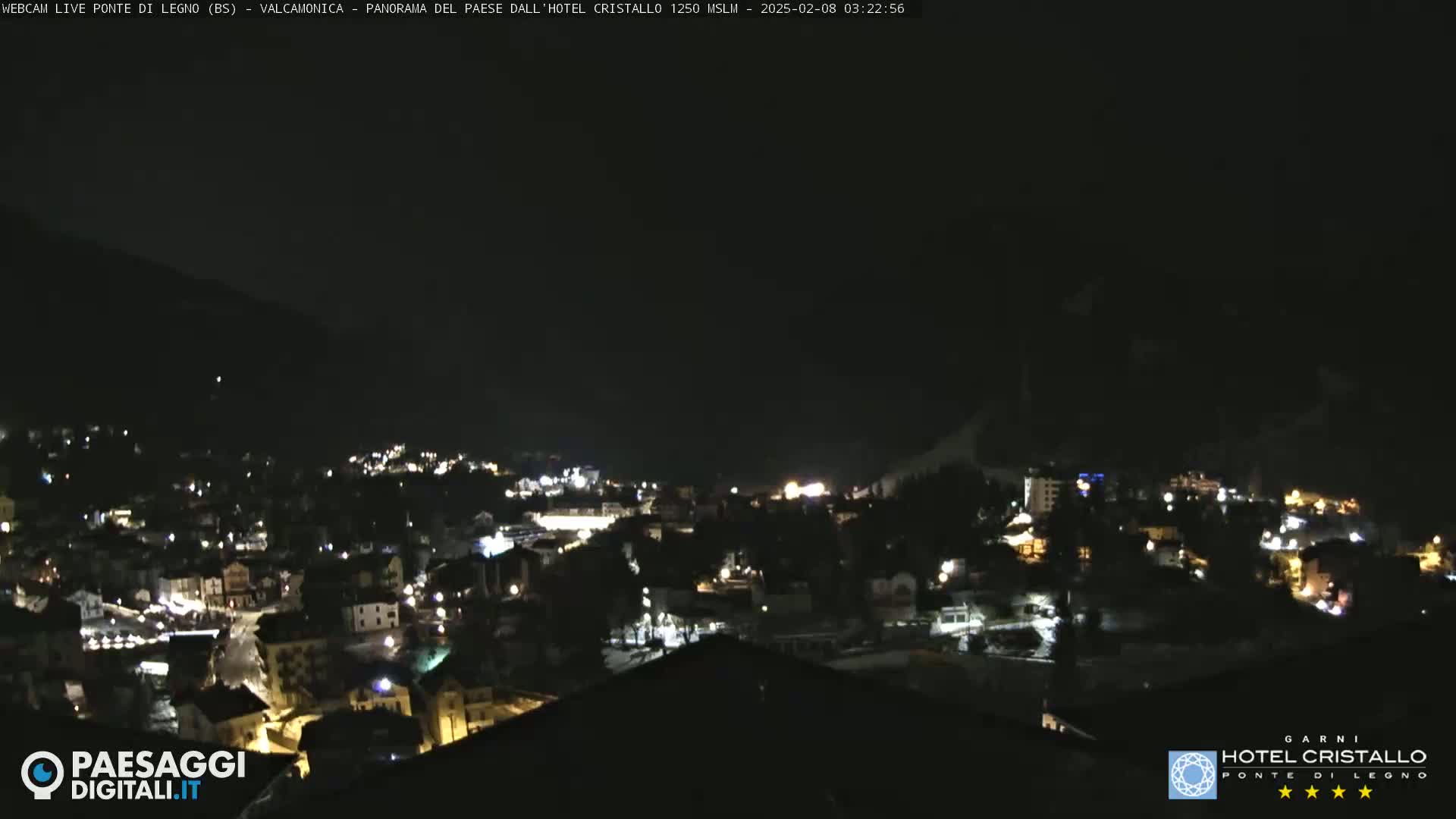 A nighttime view of a town nestled in a valley, illuminated by scattered lights under a dark, clear sky.