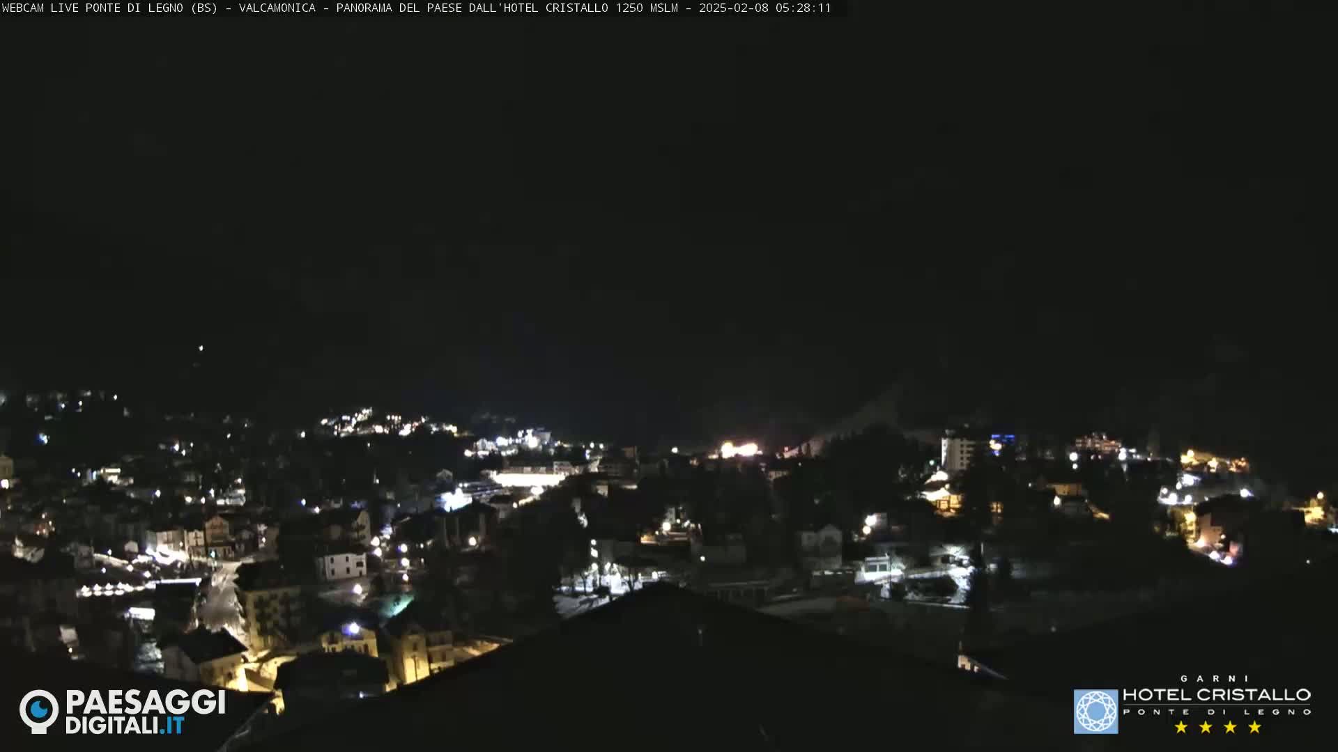 A nighttime, long shot of a town illuminated by scattered lights under a dark sky.