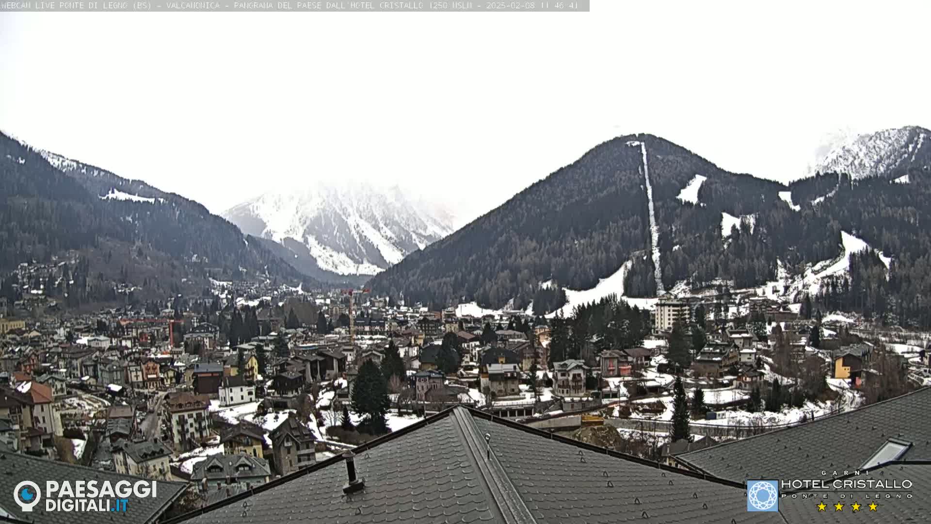A snow-dusted mountain town nestled in a valley between snow-capped mountains under an overcast sky.