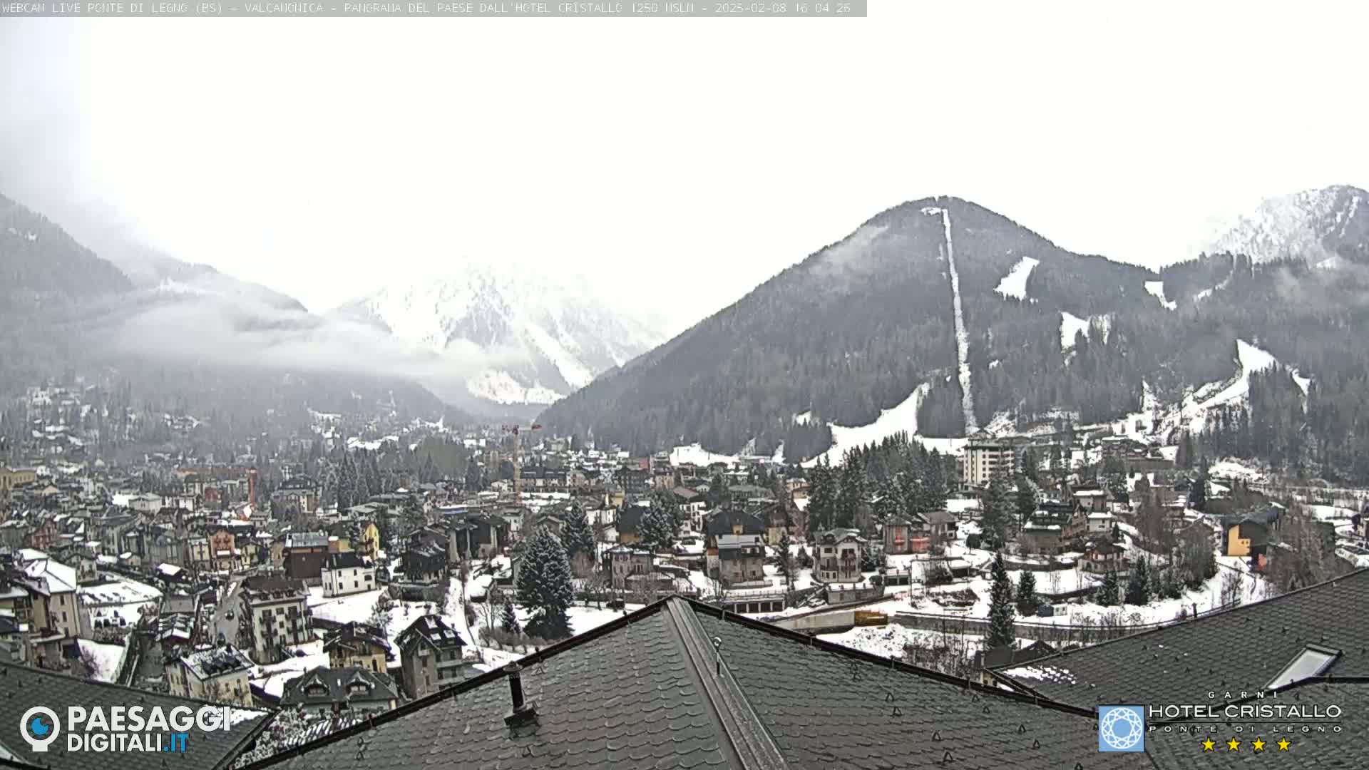 A snow-covered town nestled in a valley between snow-capped mountains under an overcast sky.