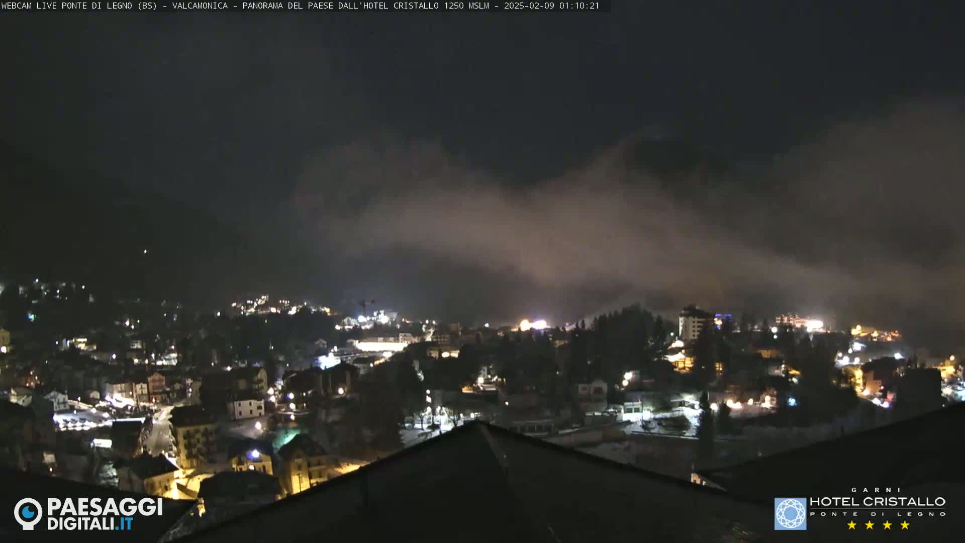 A nighttime view of a snow-dusted town nestled in a valley, partially obscured by fog or low clouds.