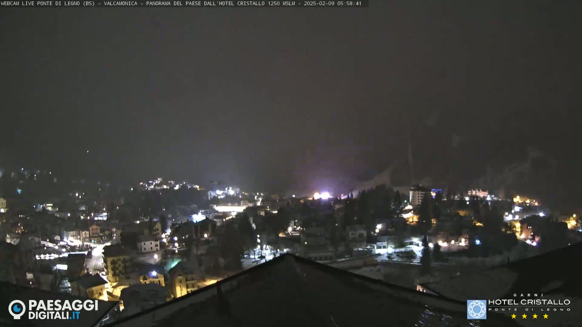 A nighttime view of a snow-covered town illuminated by lights under a dark, overcast sky.