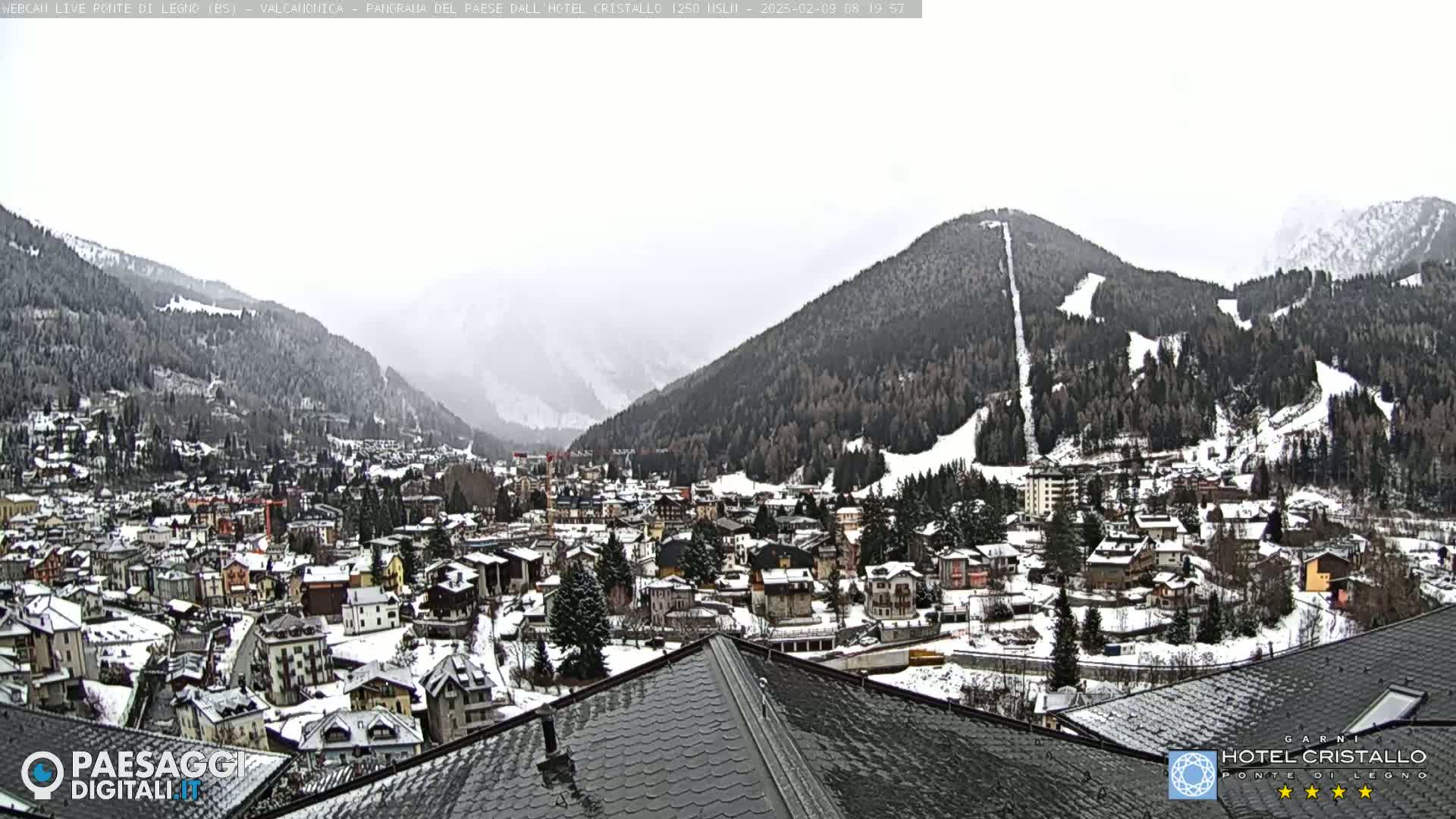 A snow-covered mountain town nestled in a valley, with snow-dusted mountains in the background under an overcast sky.