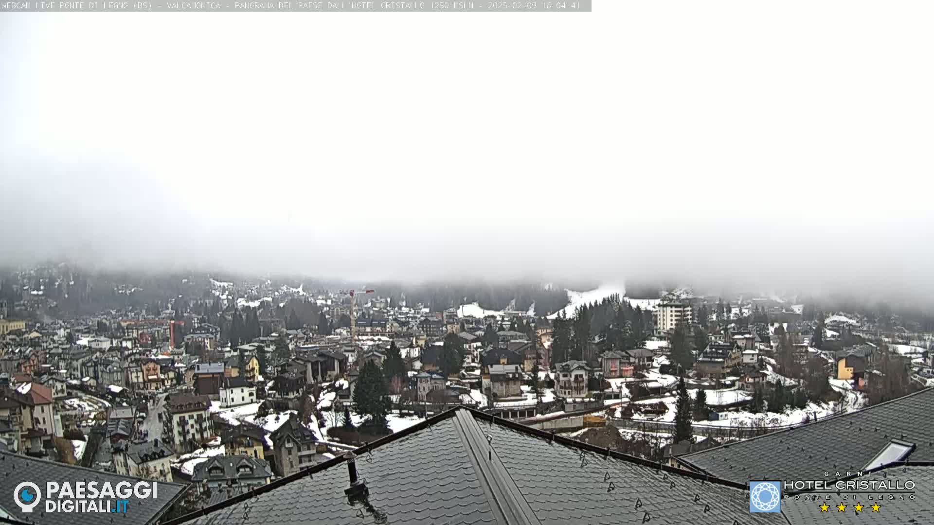 A foggy view of a snow-dusted town nestled in a valley, seen from a rooftop.