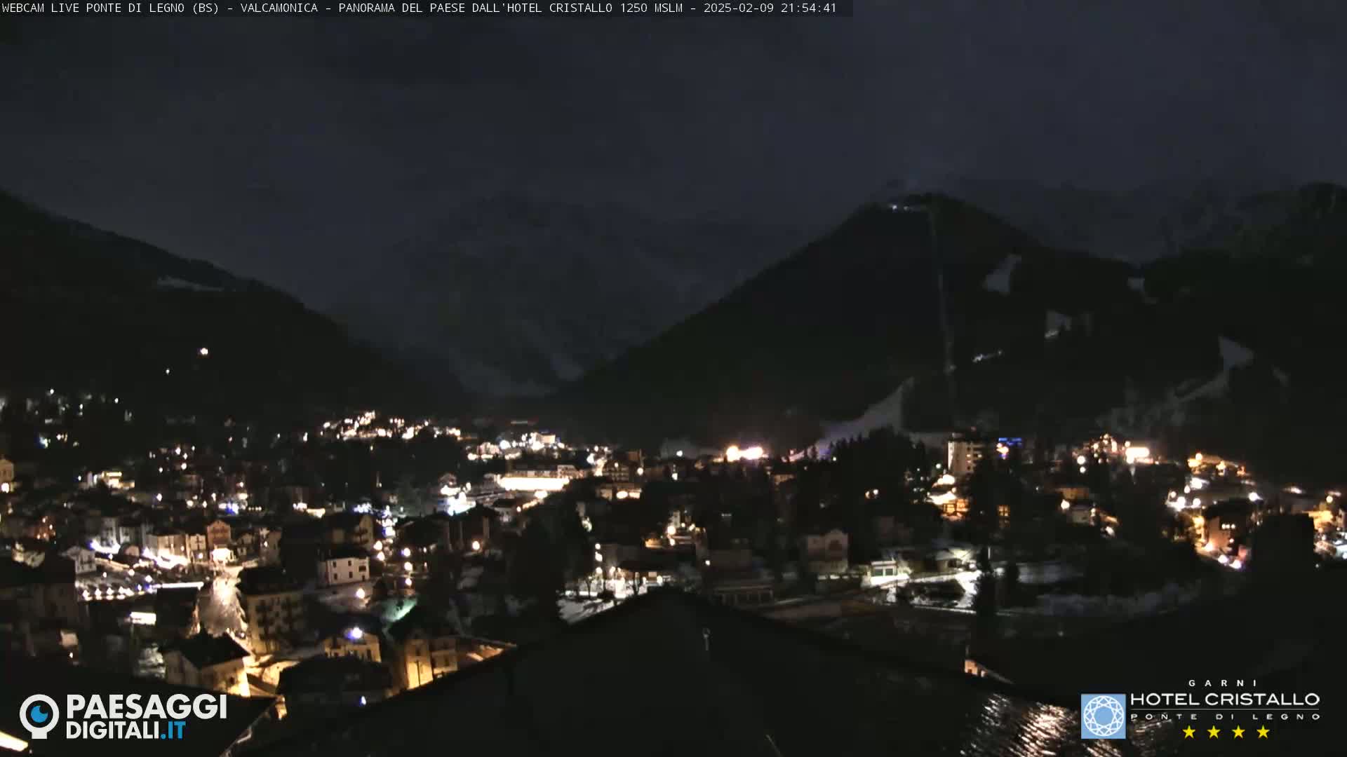 A nighttime view of a town nestled in a valley between snow-dusted mountains.