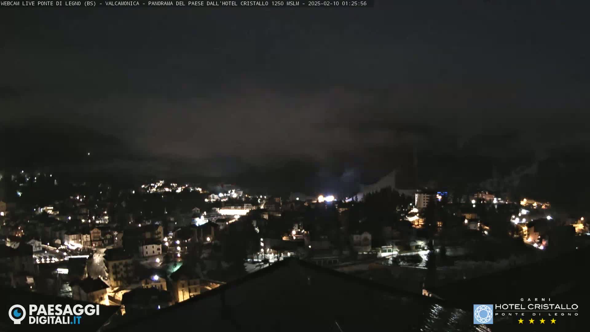 A nighttime view of a snow-covered town nestled in a valley, partially obscured by fog or low clouds.